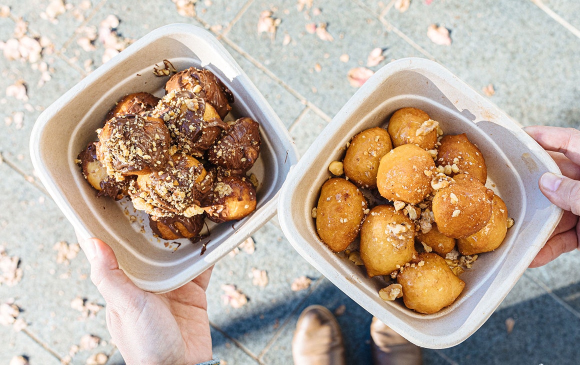 two takeaway boxes of loukoumades, one with nutella and one with honey and nuts